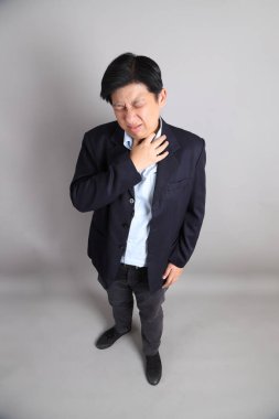 Resmi giyinmiş Asyalı iş adamı. Gri arka planda hastalıklı hareketler yapıyor..