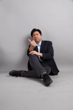 Resmi giyinmiş Asyalı iş adamı. Gri arka planda baş parmak işareti var..