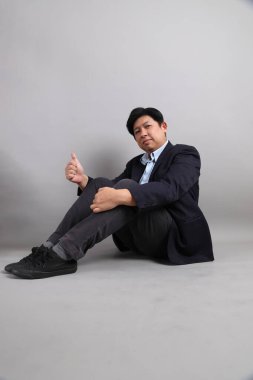 Gri arka planda otururken poz veren resmi giyinmiş Asyalı iş adamı..