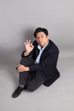 Resmi giyinmiş Asyalı iş adamı, tamam ya da gri arka planı onaylıyor..