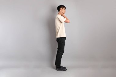 Gri arka planda giyinmiş genç Güney Asyalı. Yorgun bir jestle duruyor.. 