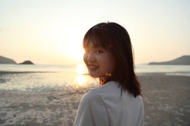 Asyalı kadın gün batımında kumsalda dinleniyor..