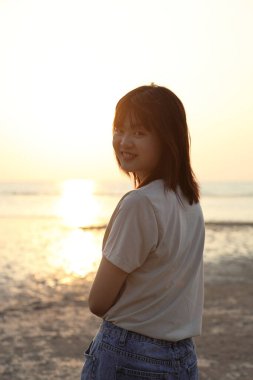 Asyalı kadın gün batımında kumsalda dinleniyor..