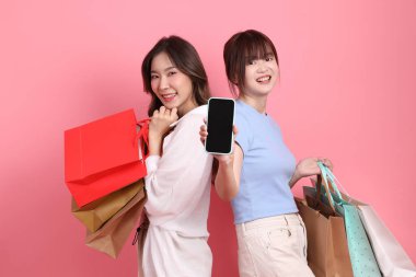 Yetişkin genç arkadaşlar, 20 'li yaşlarda pembe arka planda alışveriş çantası tutan Doğu Asyalı kadınlar.. 