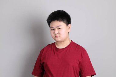 Gri arka planda duran, sıradan giyinmiş, Doğu Asyalı çocuk.. 