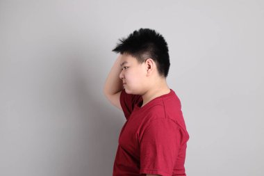 Gri arka planda düşünce jesti yapan sıradan giysili Doğu Asyalı çocuk.. 