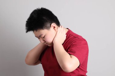 Gri arka planda yorgun jestleri olan sıradan giyinmiş Doğu Asyalı çocuk.. 