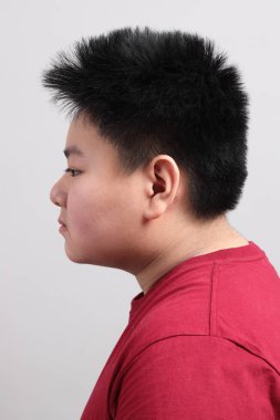 Gri arka planda duran, sıradan giyinmiş, Doğu Asyalı çocuk.. 