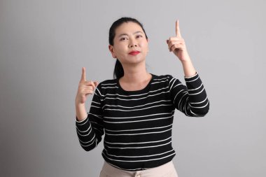 Gri arkaplanı işaret eden, günlük kıyafetler giyen 40 'lı yaşlardaki Doğu Asyalı kadın..