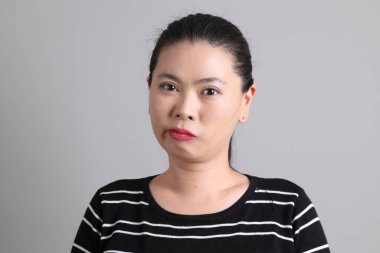 Açıklama: 40 'lı yaşlarda, gri arka planda mutsuz davranışlar sergileyen sıradan giysili Doğu Asyalı kadın..