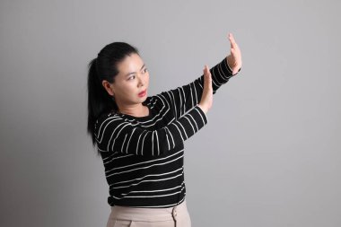 40 'lı yaşlarda, gri arka planda durmayı yasaklayan, yasaklayan ve reddeden sıradan giysili Doğu Asyalı bir kadın..