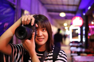 Genç Asyalı kadın Bangkok, Tayland 'da gece pazarında fotoğraf çekmekten zevk alıyor. Şehir yaşam tarzı, konaklama. Bokeh arka planda. Turist