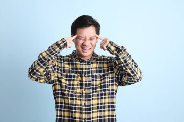 Diş teli takan, sıradan bir tişört giyen, mavi arka planda düşünme hareketi yapan Asyalı bir adam..