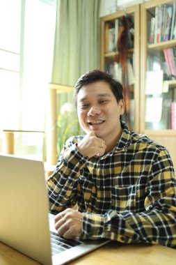 Diş teli takan Asyalı bir adam evdeki çalışma alanında dizüstü bilgisayarla çalışıyor..