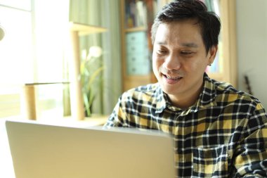 Diş teli takan Asyalı bir adam evdeki çalışma alanında dizüstü bilgisayarla çalışıyor..