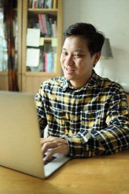 Diş teli takan Asyalı bir adam evdeki çalışma alanında dizüstü bilgisayarla çalışıyor..