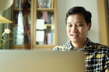 Diş teli takan Asyalı bir adam evdeki çalışma alanında dizüstü bilgisayarla çalışıyor..