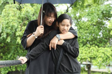 Asyalı bekar anne ve oğlu yağmur mevsiminde parkta birlikte vakit geçiriyorlar..