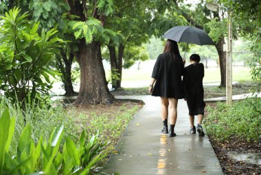 Asyalı bekar anne ve oğlu yağmur mevsiminde parkta birlikte vakit geçiriyorlar..