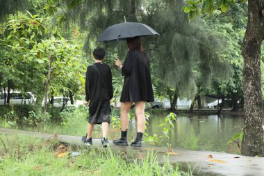 Asyalı bekar anne ve oğlu yağmur mevsiminde parkta birlikte vakit geçiriyorlar..