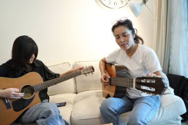 Asyalı bekar anne, kızına oturma odasında gitar çalmayı öğretiyor..