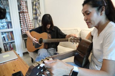 Asyalı bekar anne, kızına oturma odasında gitar çalmayı öğretiyor..