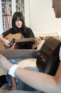 Asyalı bekar anne, kızına oturma odasında gitar çalmayı öğretiyor..