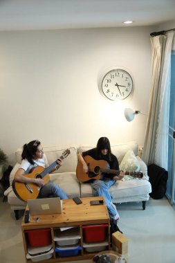 Asyalı bekar anne, kızına oturma odasında gitar çalmayı öğretiyor..