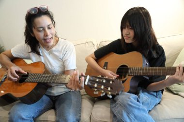 Asyalı bekar anne, kızına oturma odasında gitar çalmayı öğretiyor..