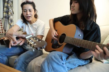 Asyalı bekar anne, kızına oturma odasında gitar çalmayı öğretiyor..