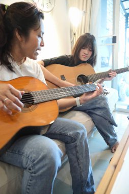 Asyalı bekar anne, kızına oturma odasında gitar çalmayı öğretiyor..