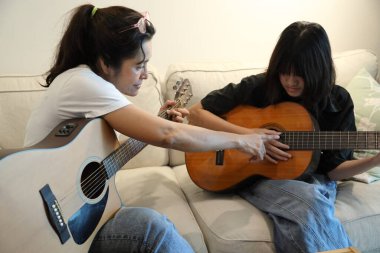 Asyalı bekar anne, kızına oturma odasında gitar çalmayı öğretiyor..