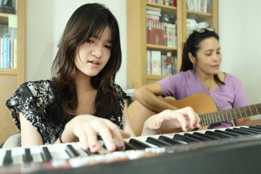 The Asian single mother playing music with her daughter. clipart