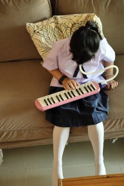 The East Asian kid practicing melodion after the school. clipart