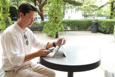 40 yaşındaki Asyalı işadamı gündüz vakti açık bir yerde tablet üzerinde çalışıyor..