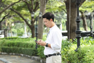 40 yaşındaki Asyalı işadamı park yerinde gündüz vakti akıllı telefon kullanarak yürüyor..