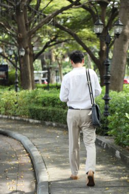 40 yaşındaki Asyalı işadamı park yerinde gündüz vakti akıllı telefon kullanarak yürüyor..