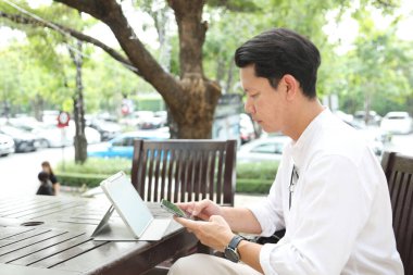 40 yaşındaki Asyalı işadamı gündüz vakti açık bir yerde tablet üzerinde çalışıyor..