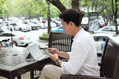 40 yaşındaki Asyalı işadamı gündüz vakti açık bir yerde tablet üzerinde çalışıyor..