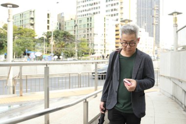 Akıllı telefon kullanan üst düzey bir Asyalı işadamı iş alanında yürüyor..