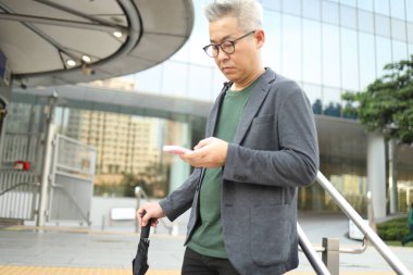 Akıllı telefon kullanan üst düzey bir Asyalı işadamı iş alanında yürüyor..