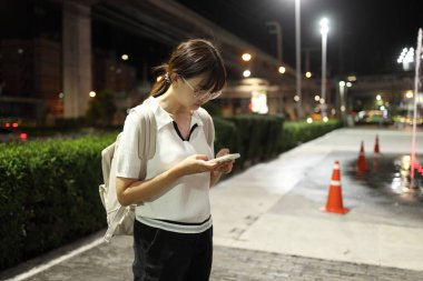 Geceleri şehirde akıllı telefon kullanan Doğu Asyalı genç kadın..