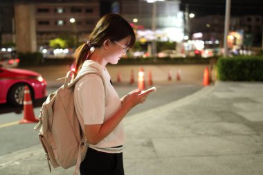 Geceleri şehirde akıllı telefon kullanan Doğu Asyalı genç kadın..