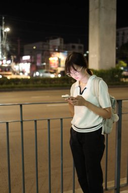 Geceleri şehirde akıllı telefon kullanan Doğu Asyalı genç kadın..