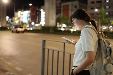 Geceleri şehirde akıllı telefon kullanan Doğu Asyalı genç kadın..