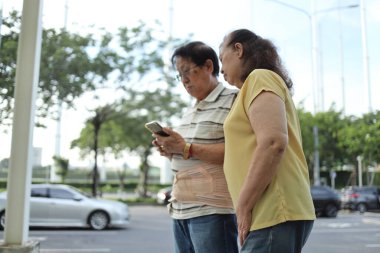 Üst düzey Asyalı adam, bel desteği kemeri takıyor ve akıllı telefon tutuyor, gün içinde karısıyla parkta yürüyor..