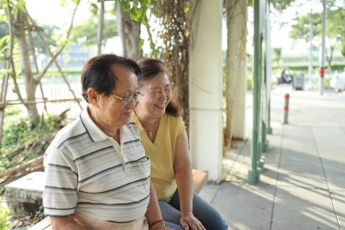 Üst düzey Asyalı çift gün boyunca parkta bankta birlikte oturuyorlar..