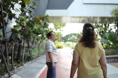 Bel destek kemeri takan kıdemli Asyalı adam gün içinde karısıyla parkta yürüyor..