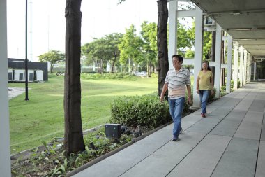Bel destek kemeri takan kıdemli Asyalı adam gün içinde karısıyla parkta yürüyor..