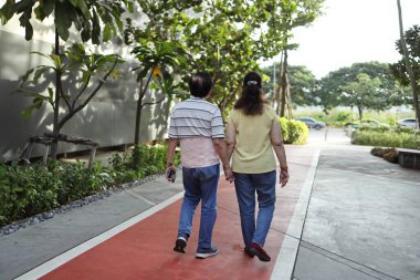 Bel destek kemeri takan kıdemli Asyalı adam gün içinde karısıyla parkta yürüyor..